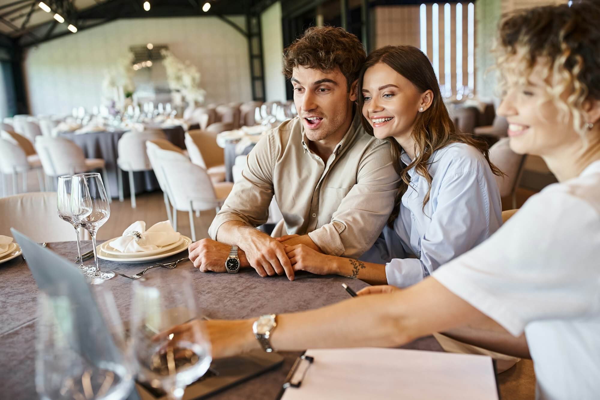 amazed-and-happy-couple-looking-at-laptop-near-event-organizer-at-festive-table-bridal-preparation.jpg