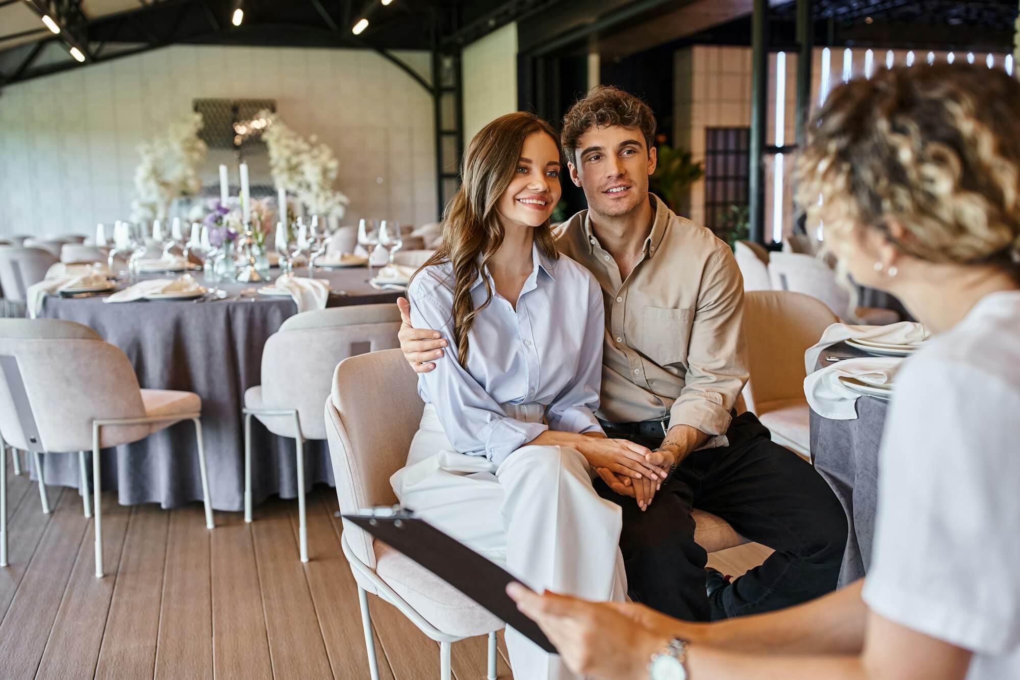 banquet-organizer-with-clipboard-talking-to-couple-in-love-in-event-hall-with-wedding-decor.jpg