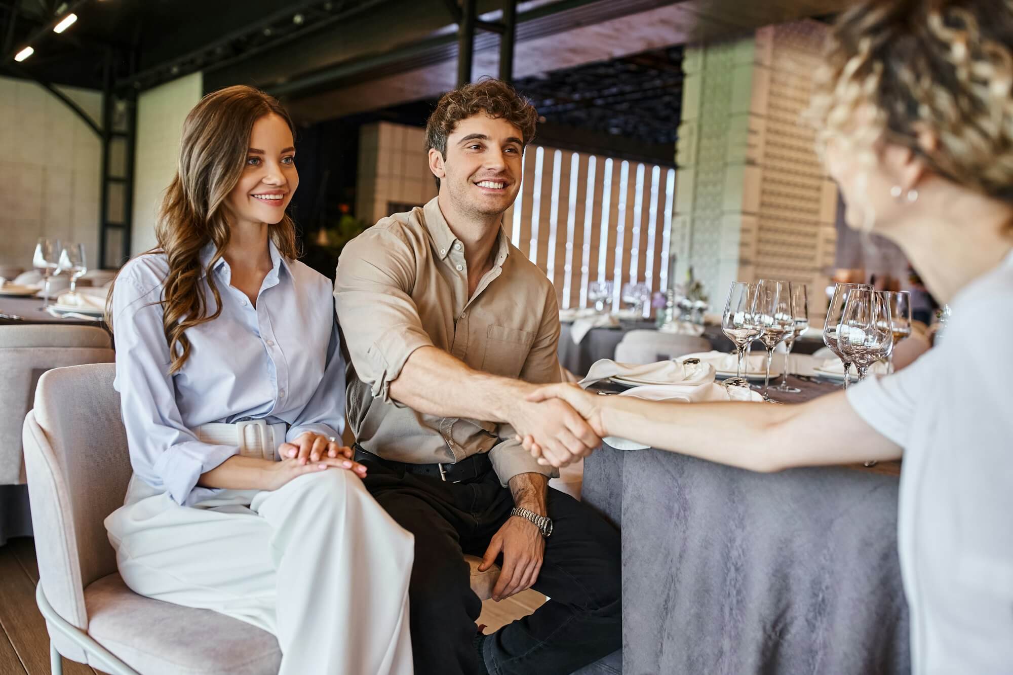 happy-man-shaking-hands-with-event-manager-near-smiling-girlfriend-at-festive-table-in-event-hall.jpg